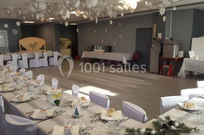 Salle de réception lumineuse avec tables dressées, nappes blanches et serviettes bleues, prête pour un événement.