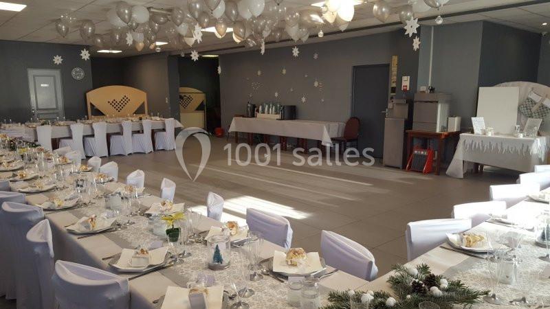 Salle de réception décorée avec des tables dressées, nappes blanches et ornements suspendus pour un événement festif.