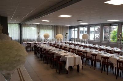Salle de réception lumineuse avec tables dressées, nappes blanches et serviettes bleues, prête pour un événement.
