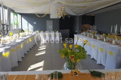 Salle de réception lumineuse avec tables dressées, nappes blanches et serviettes bleues, prête pour un événement.