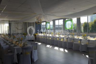 Salle de réception lumineuse avec tables dressées, nappes blanches et serviettes bleues, prête pour un événement.