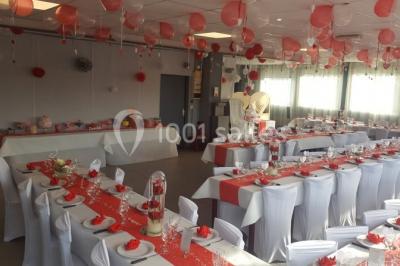 Salle de réception lumineuse avec tables dressées, nappes blanches et serviettes bleues, prête pour un événement.