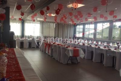 Salle de réception lumineuse avec tables dressées, nappes blanches et serviettes bleues, prête pour un événement.
