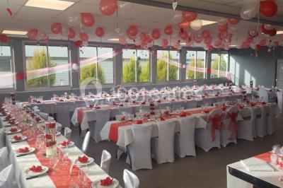 Salle de réception lumineuse avec tables dressées, nappes blanches et serviettes bleues, prête pour un événement.