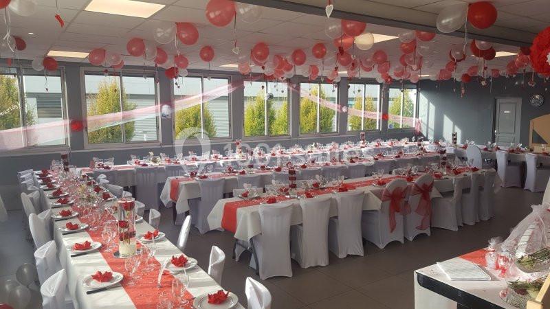 Salle décorée en rouge et blanc avec des tables dressées pour un événement festif, ornée de ballons et de nappes colorées.