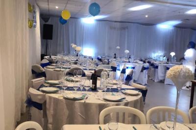 Salle de réception lumineuse avec tables dressées, nappes blanches et serviettes bleues, prête pour un événement.