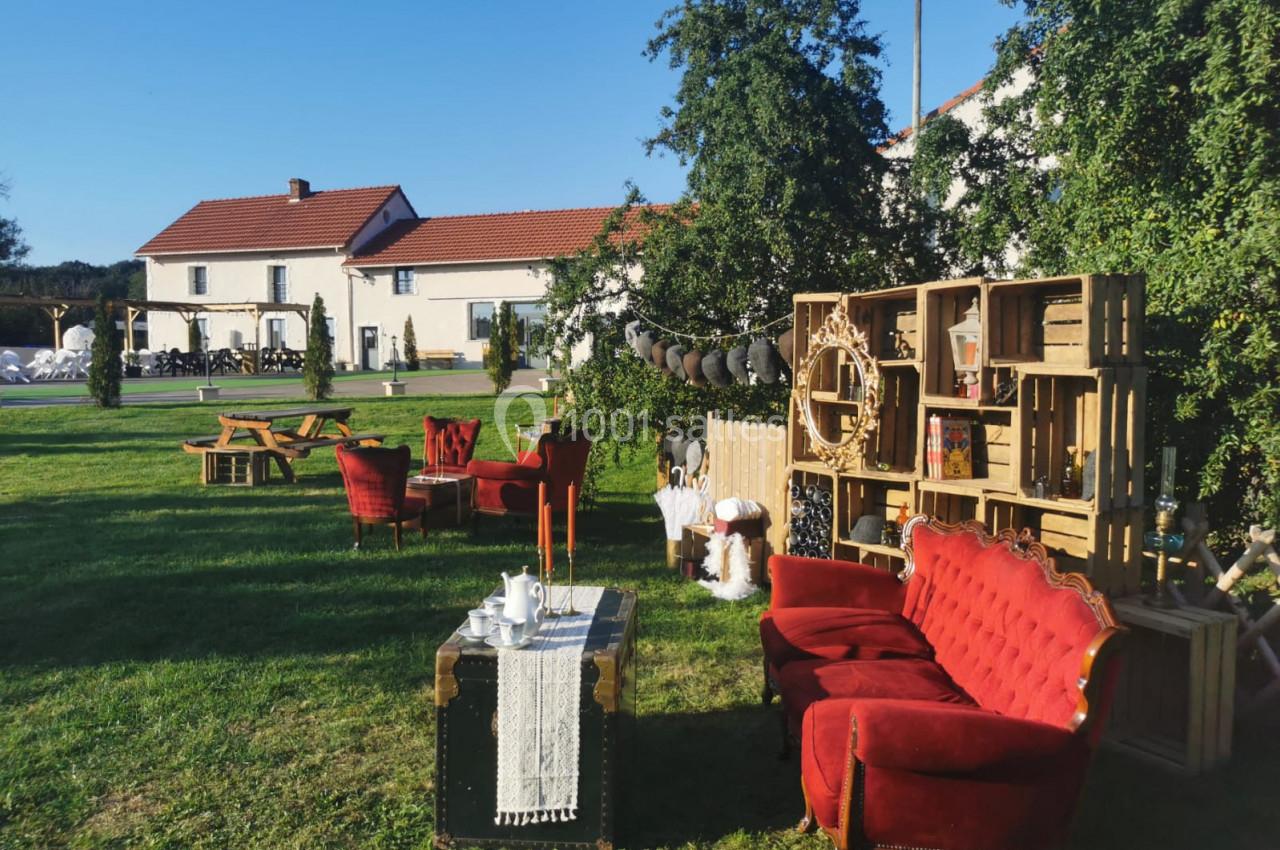 Mobilier vintage avec fauteuils rouges et décorations en bois disposés sur une pelouse devant des bâtiments.
