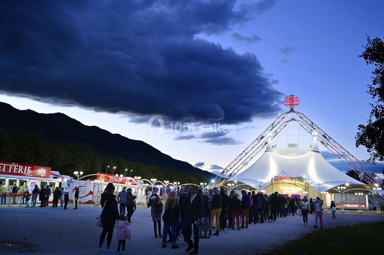 Foule faisant la queue devant un chapiteau illuminé au crépuscule, avec des montagnes en arrière-plan.