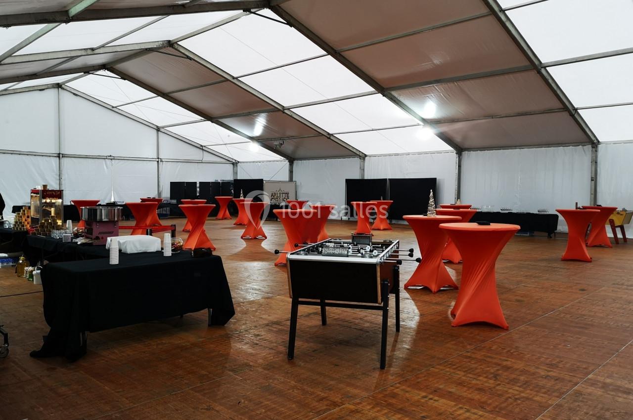 Grande tente aménagée avec des tables hautes recouvertes de nappes rouges, un baby-foot et des buffets noirs.