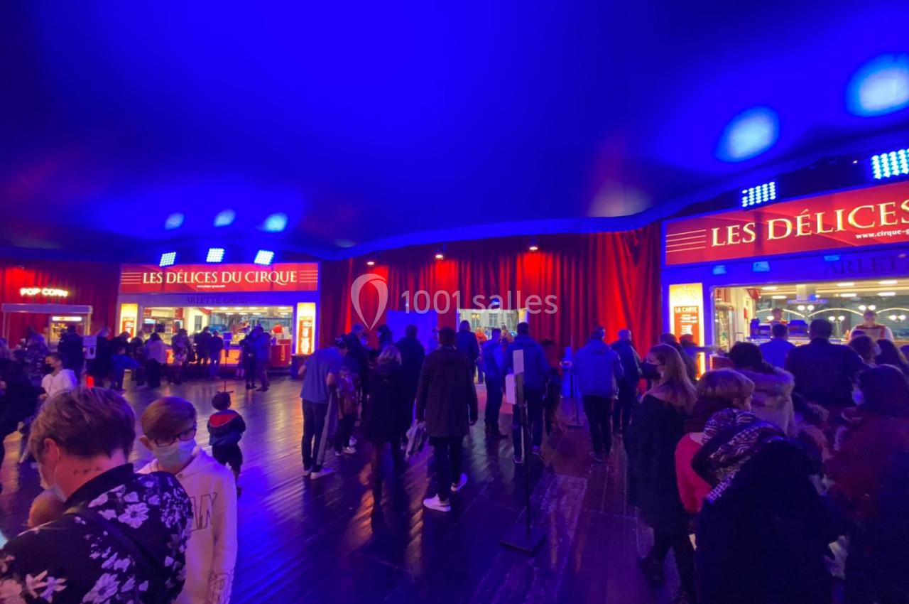 Foule rassemblée sous un chapiteau éclairé en bleu, devant des stands de restauration aux enseignes lumineuses.