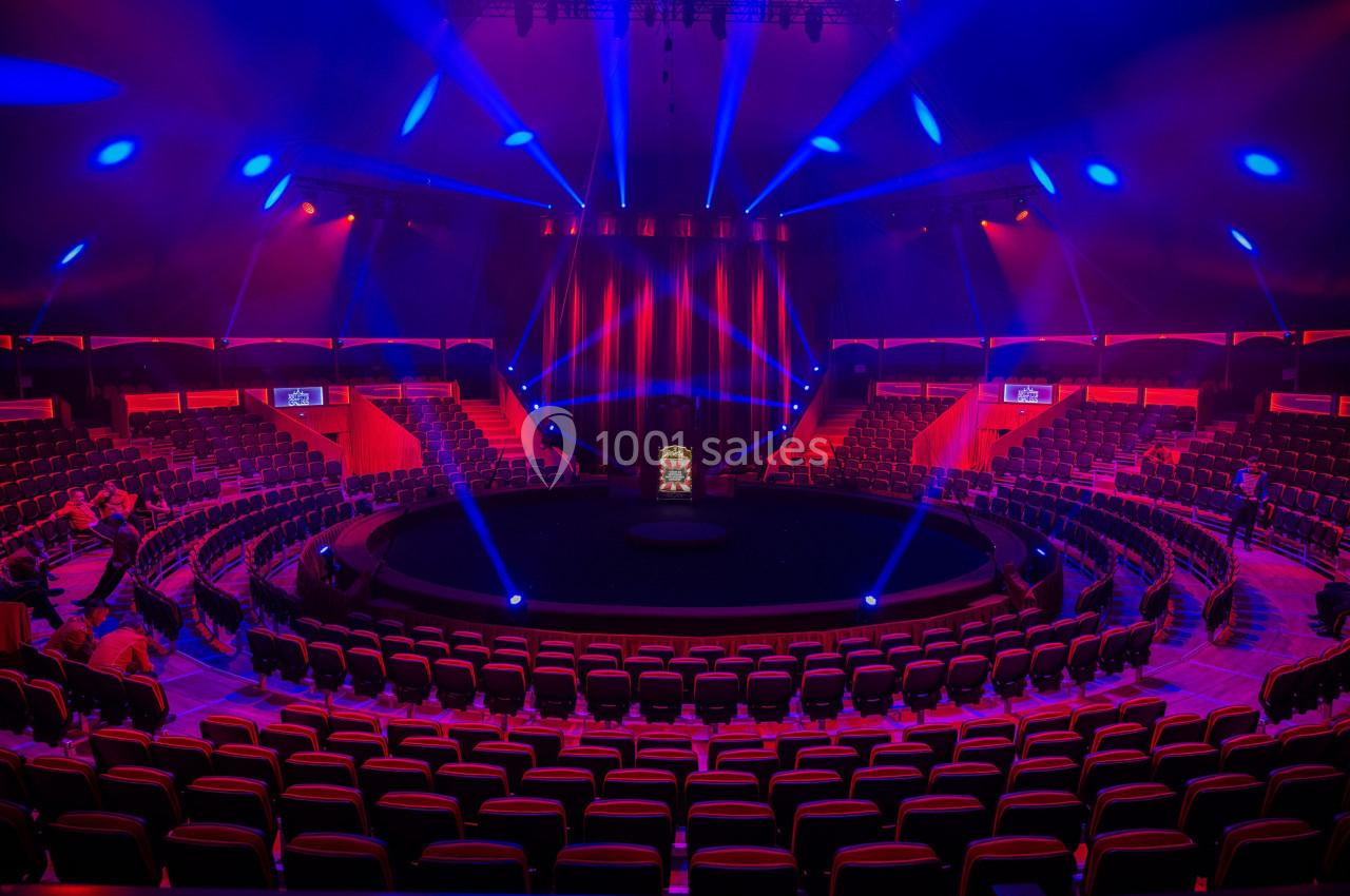 Gradins circulaires illuminés de lumières rouges et bleues entourant une scène centrale dans une salle de spectacle.