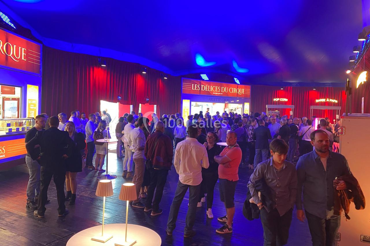 Foule rassemblée dans un chapiteau éclairé, près de stands de restauration et de boissons.