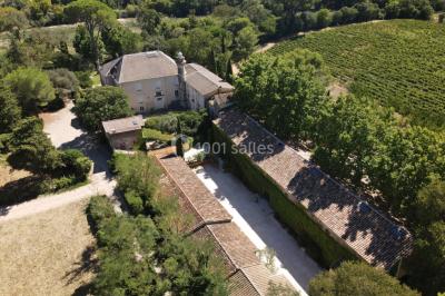 Façade d'une grande maison blanche entourée d'arbres, avec une pelouse verdoyante au premier plan.