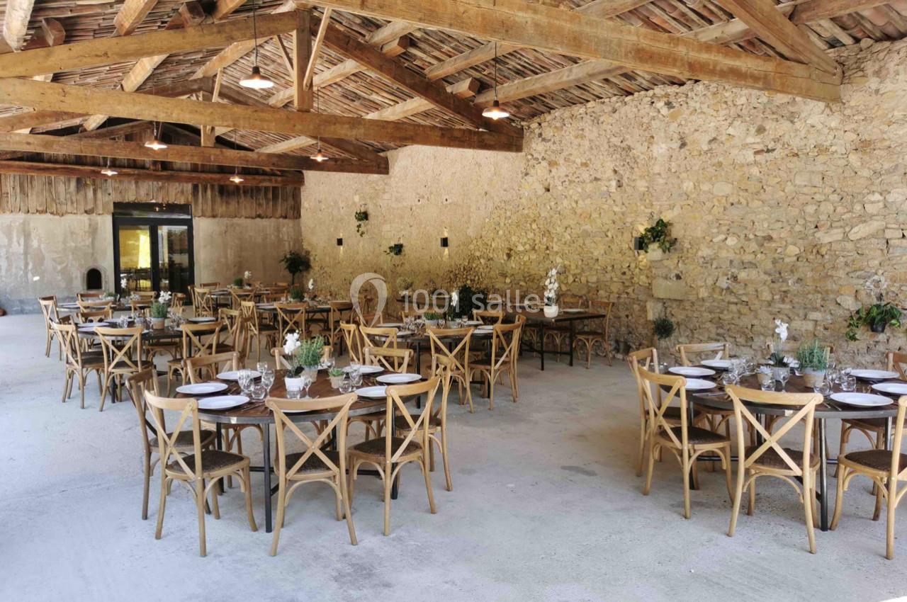 Salle de réception rustique avec murs en pierre, poutres apparentes et tables en bois dressées pour un événement.
