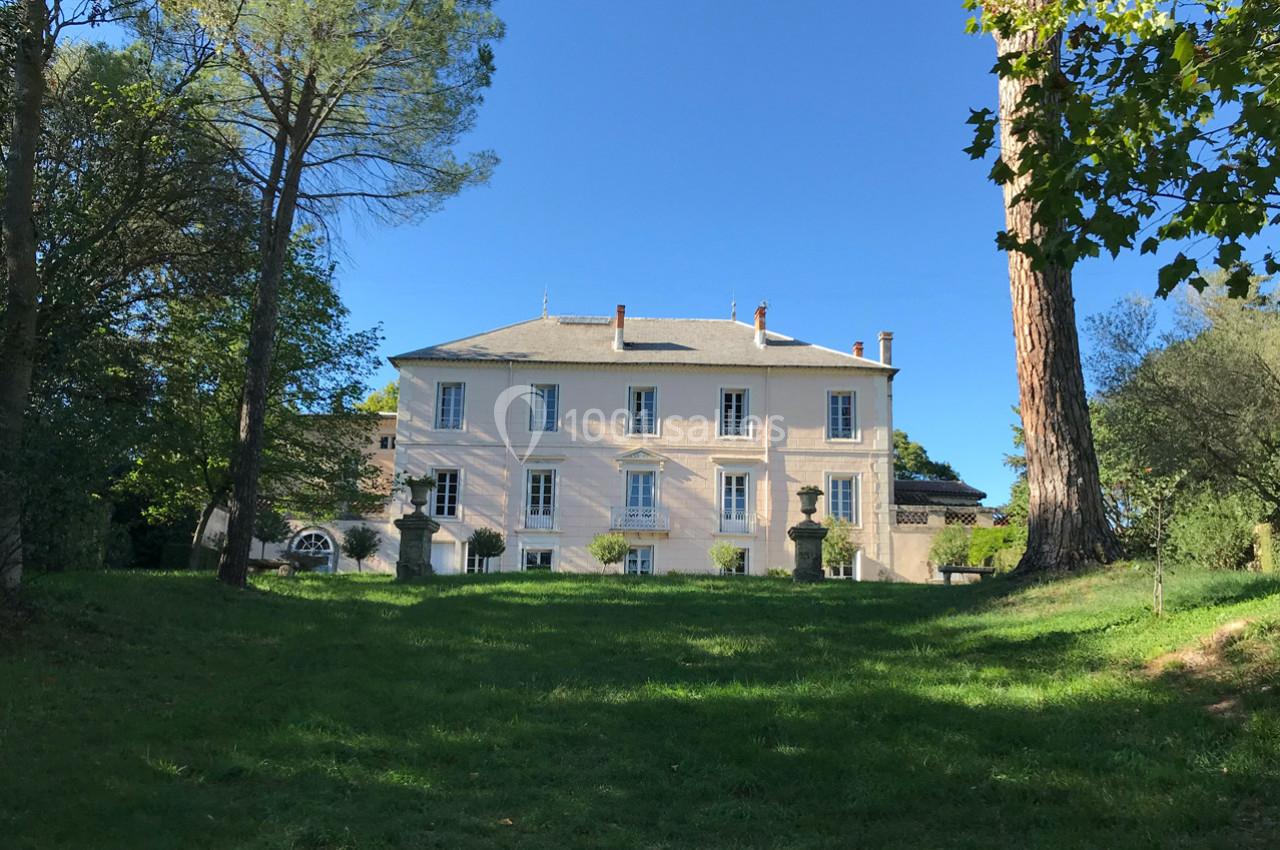 Façade d'une grande maison blanche entourée d'arbres, avec une pelouse verdoyante au premier plan.