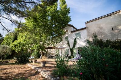 Façade d'une grande maison blanche entourée d'arbres, avec une pelouse verdoyante au premier plan.