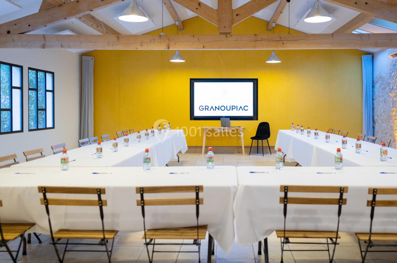 Salle de réunion lumineuse avec tables disposées en U, écran de présentation allumé et bouteilles d'eau sur les tables.