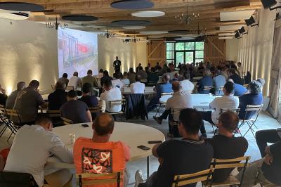 Façade d'une grande maison blanche entourée d'arbres, avec une pelouse verdoyante au premier plan.