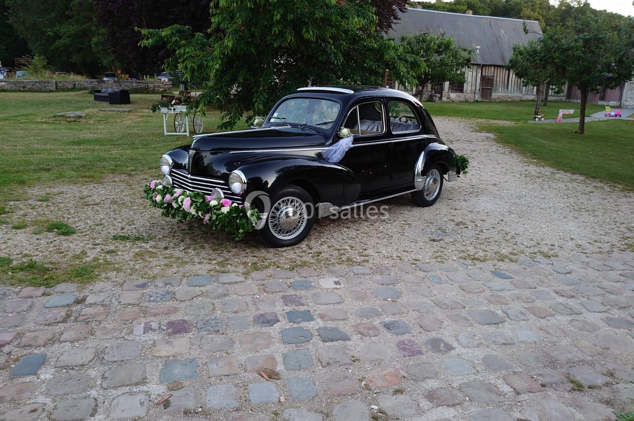 Voiture ancienne noire décorée de fleurs, stationnée sur une allée pavée dans un cadre champêtre.