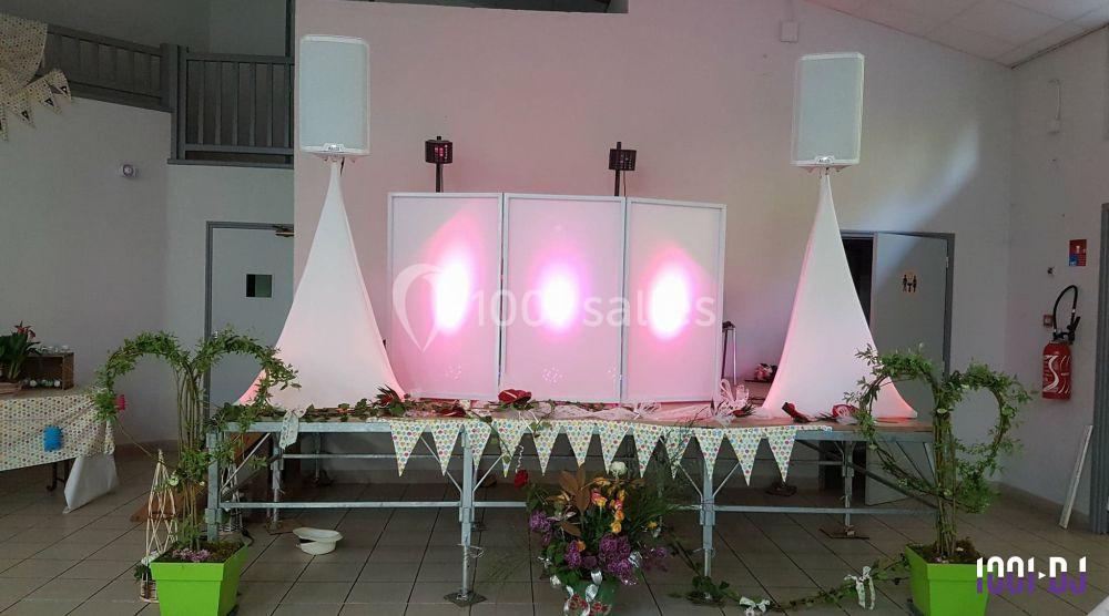 Installation de matériel de sonorisation et éclairage sur une scène décorée avec des guirlandes et des plantes.