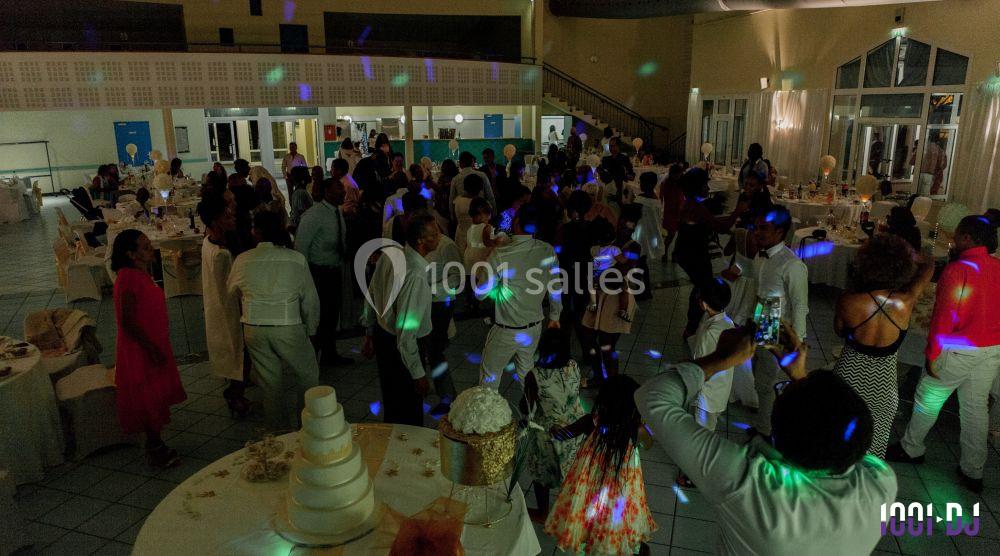 Salle de réception animée avec des invités dansant sous des lumières colorées, tables décorées en arrière-plan.