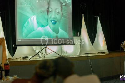 Salle de réception avec tables dressées, nappes blanches, chaises décorées et éclairage naturel à travers de grandes…