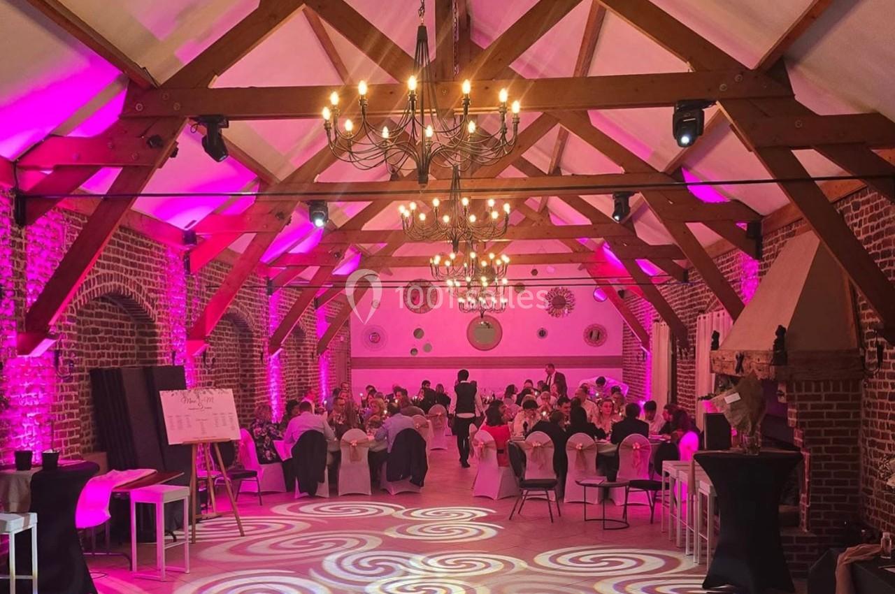 Traiteur Forest-sur-Marque (Nord) - Auberge du Tilleul #14 Salle de réception en briques avec poutres apparentes, éclairée par des lumières roses et des lustres, tables dressées.
