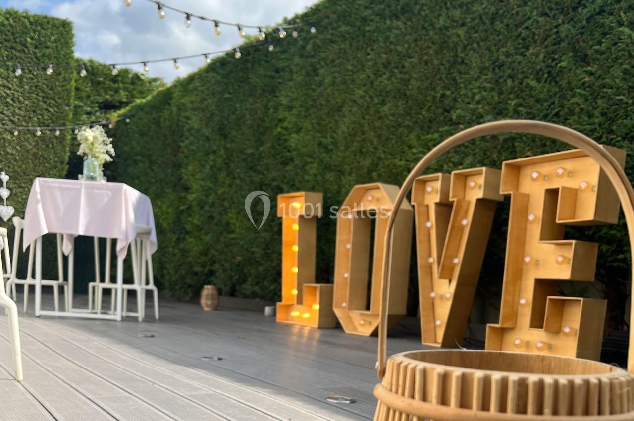 Traiteur Forest-sur-Marque (Nord) - Auberge du Tilleul #12 Décoration extérieure avec grandes lettres lumineuses ’LOVE’, table haute blanche et guirlandes suspendues, devant une haie.