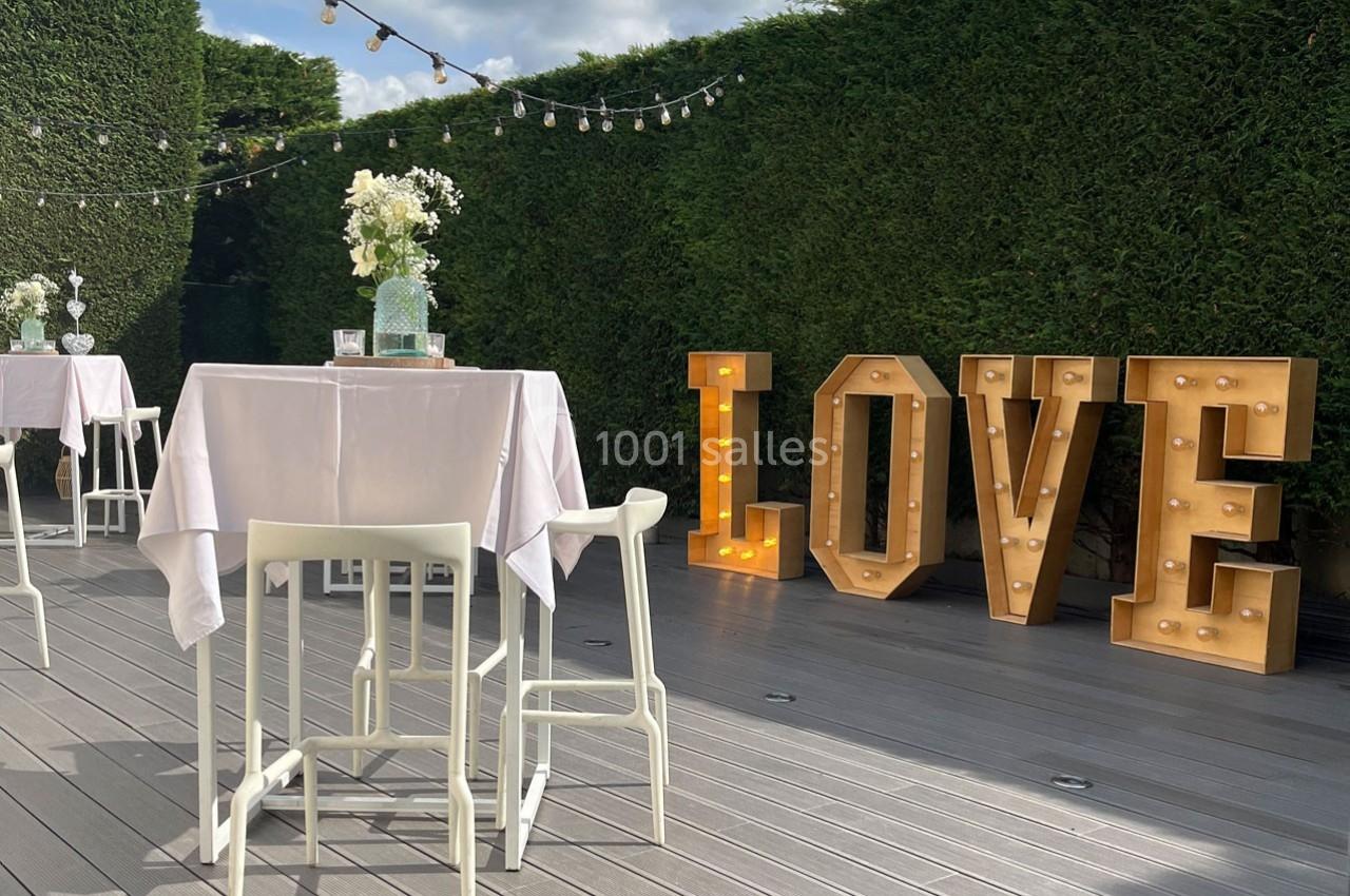 Traiteur Forest-sur-Marque (Nord) - Auberge du Tilleul #9 Terrasse décorée avec des tables hautes, guirlandes lumineuses et lettres géantes ’LOVE’ éclairées devant une haie.
