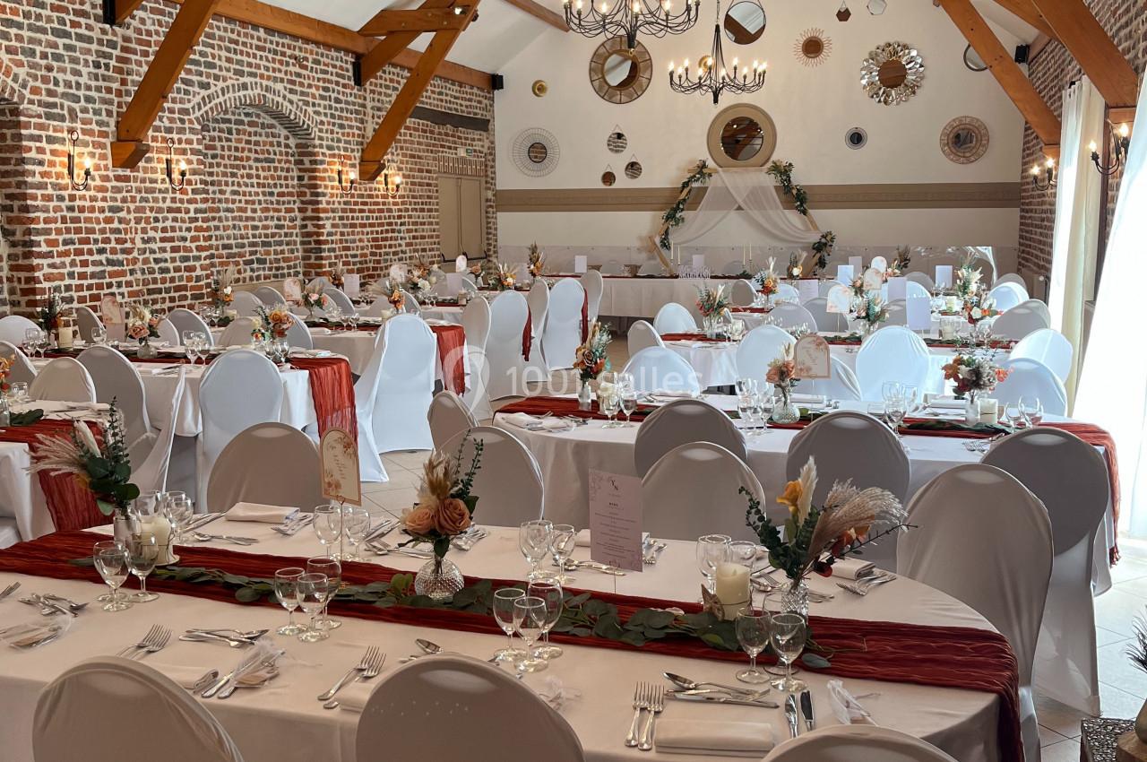 SALON GAUGUIN ET SON MUR DE MIROIRS Salle de réception décorée avec des tables dressées, nappes blanches, centres de table floraux et poutres apparentes.