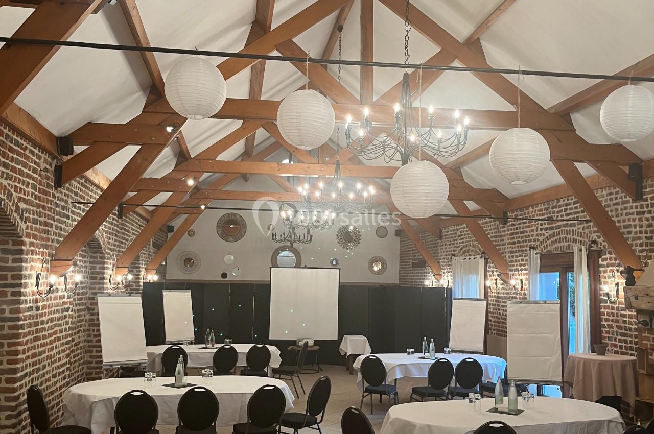 SEMINAIRE Salle de réunion spacieuse avec poutres apparentes, tables rondes et rectangulaires, chaises noires et décorations…