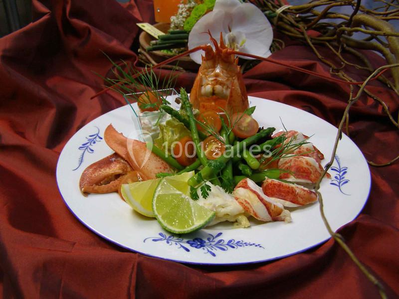 Assiette de fruits de mer avec homard, asperges, tomates cerises, citron vert et décorations sur une nappe rouge.