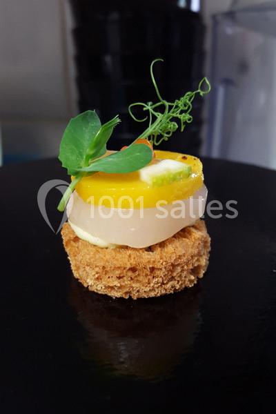 Bouchée gastronomique composée de pain croustillant, poisson, crème, gelée jaune et décoration végétale.