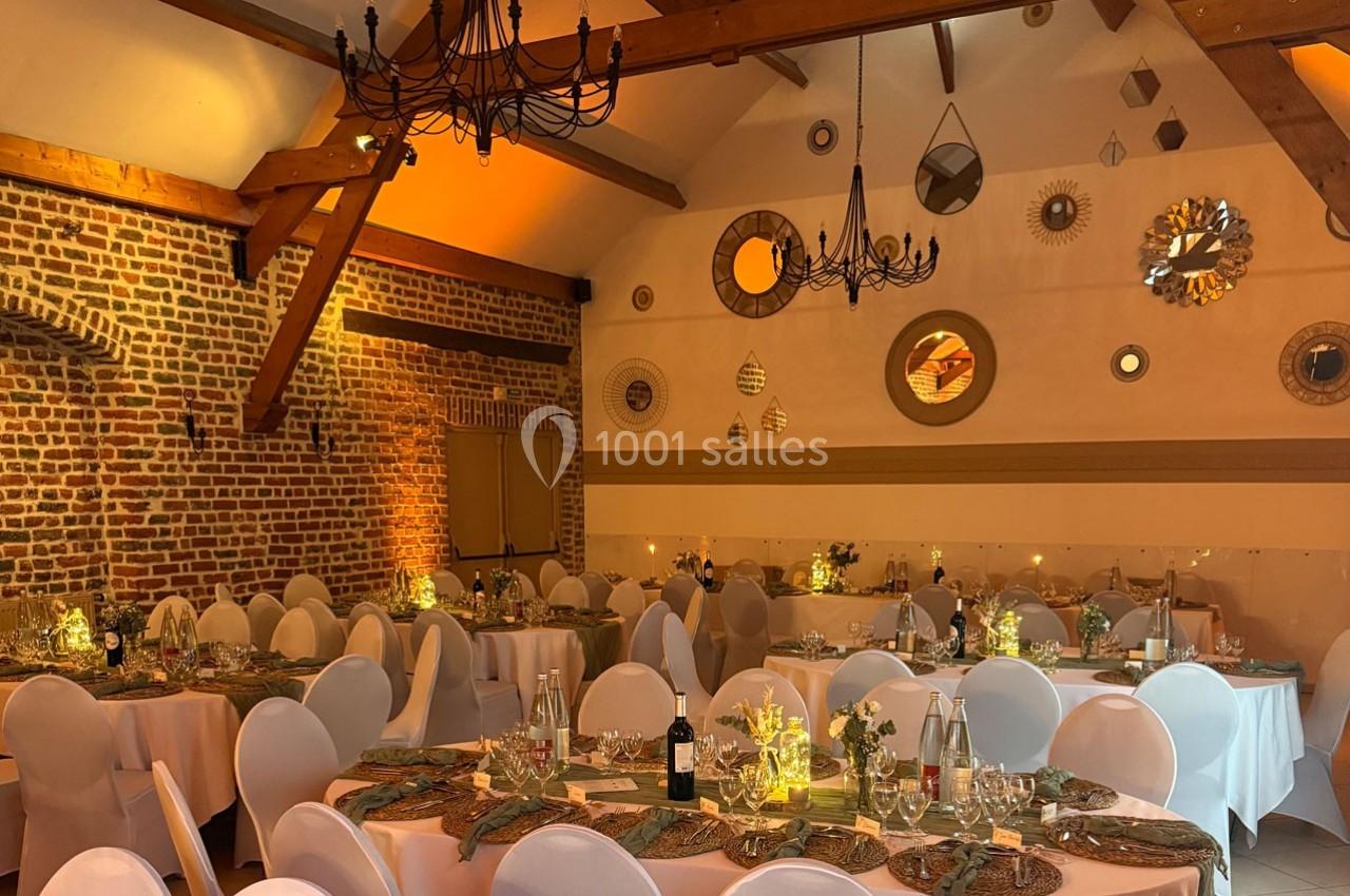 Salle de réception décorée avec des tables dressées, des chaises blanches et des lumières tamisées sous un plafond en…