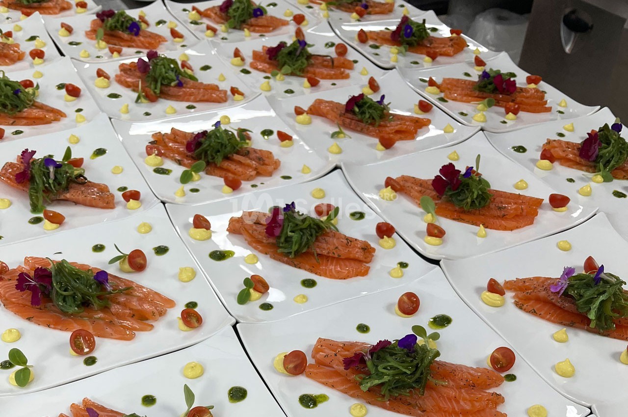 Assiettes de saumon fumé garnies de tomates cerises, algues, fleurs comestibles et sauces colorées.