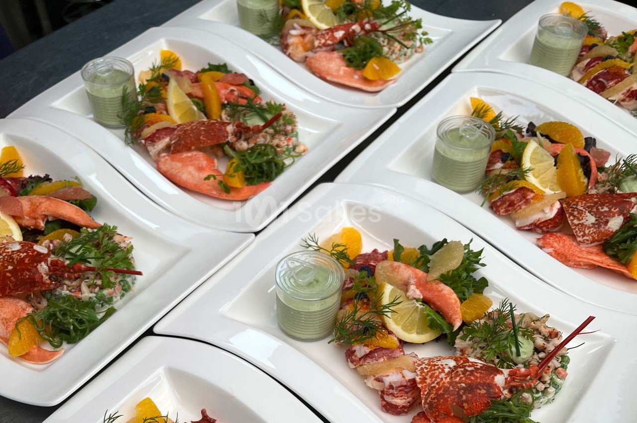 Assiettes de fruits de mer avec homard, saumon, agrumes, salade verte et sauce servies sur des plateaux blancs.