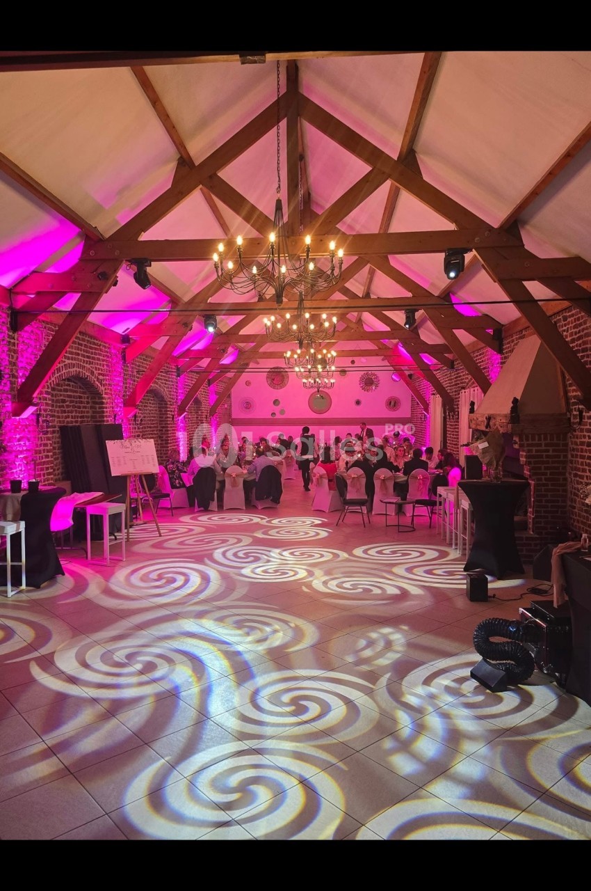 Salle de réception avec charpente en bois, éclairage rose et motifs lumineux projetés au sol.