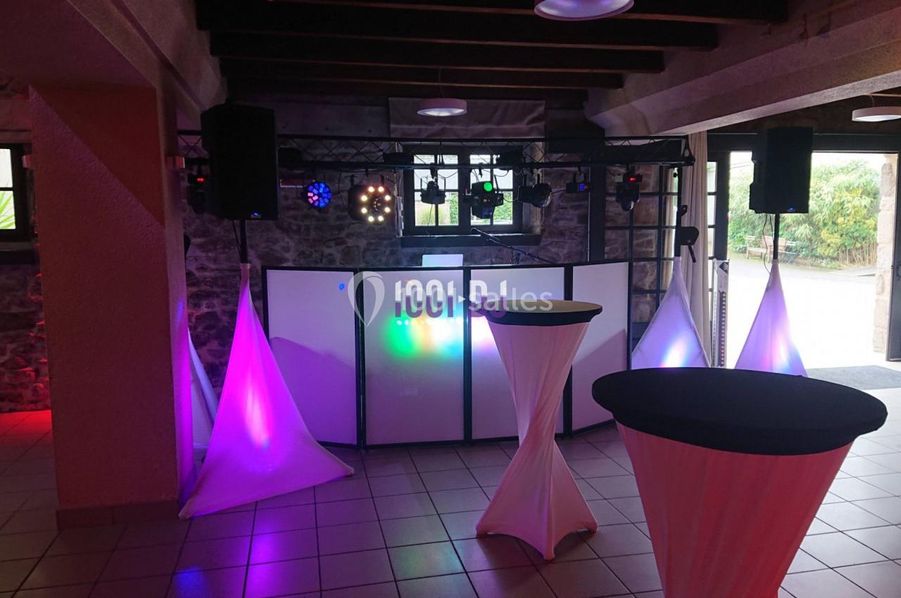 Installation de matériel de sonorisation et éclairage dans une salle avec tables hautes habillées de nappes blanches.