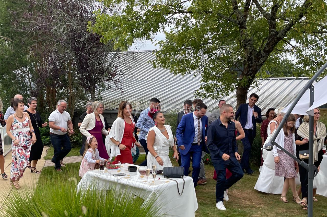 Groupe de personnes dansant en extérieur lors d'une fête, près d'une table dressée et sous des arbres.
