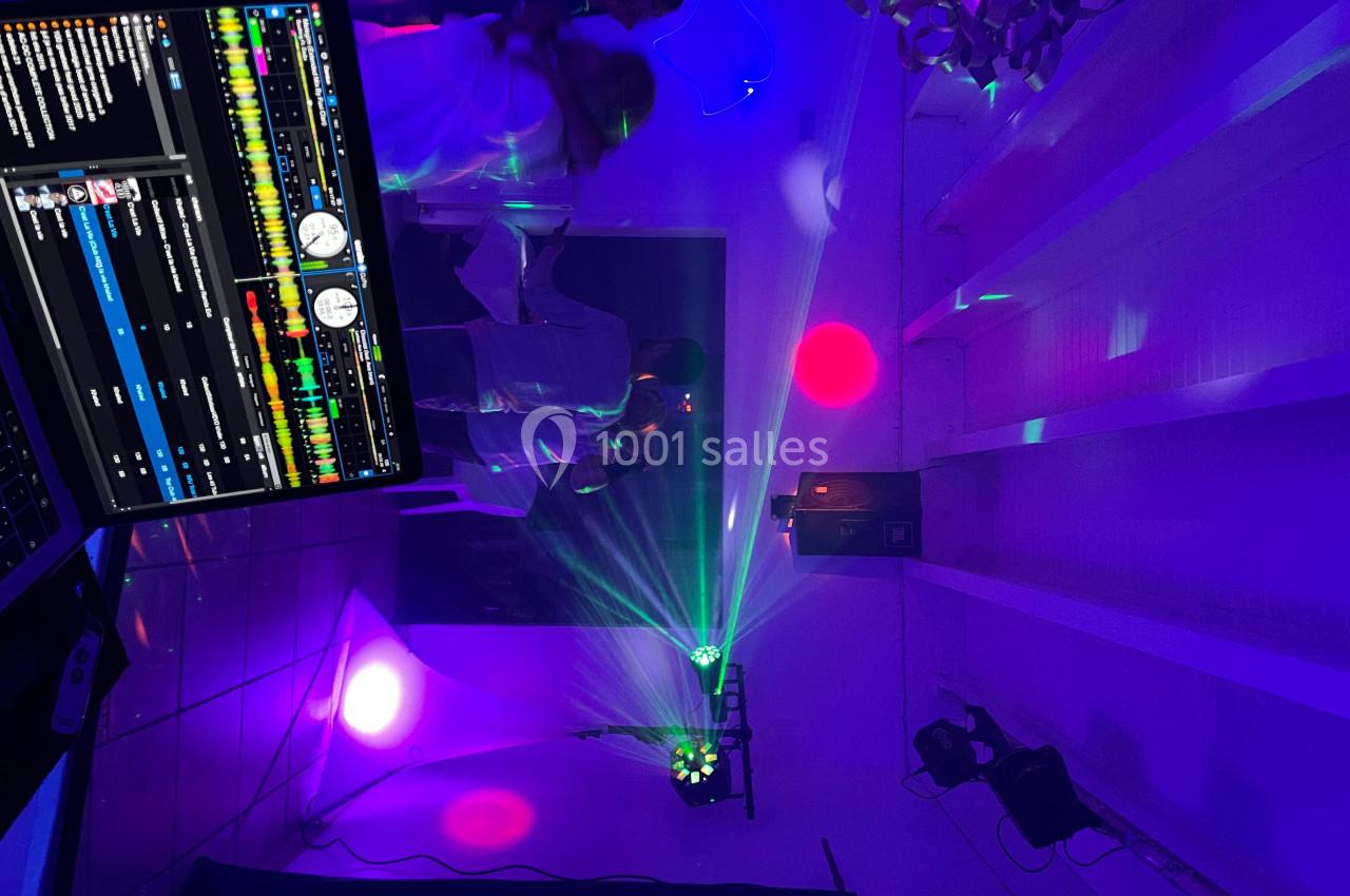 Salle de fête éclairée par des lumières colorées, avec une table de mixage visible au premier plan.