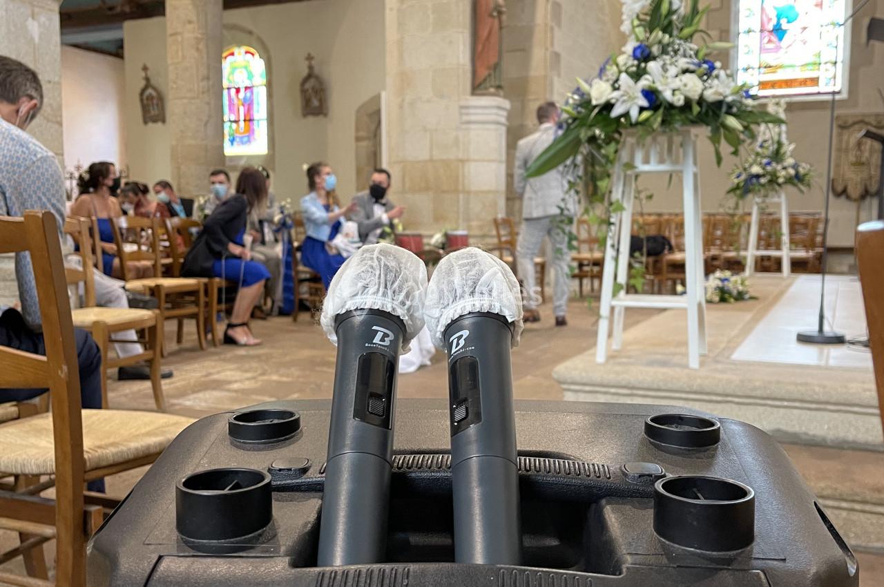 Deux micros sans fil posés sur une enceinte dans une église, avec des invités assis et des décorations florales en arrière…