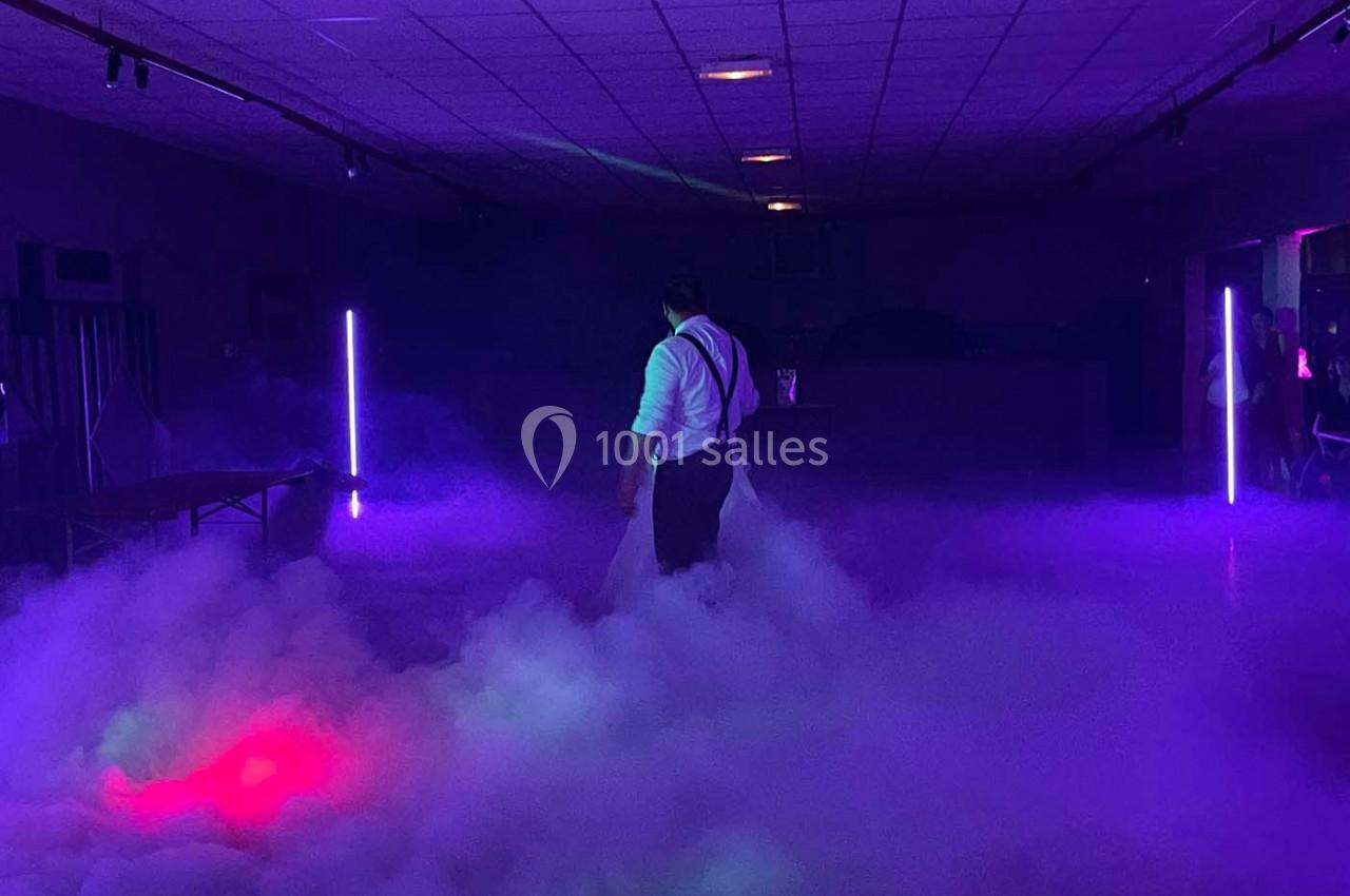 Un homme marche dans une salle sombre éclairée par des lumières violettes et entourée de fumée dense.