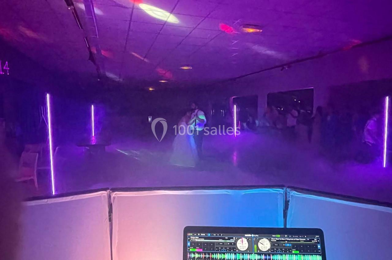 Un couple danse sous des lumières violettes dans une salle sombre, vu depuis une table de mixage de DJ.