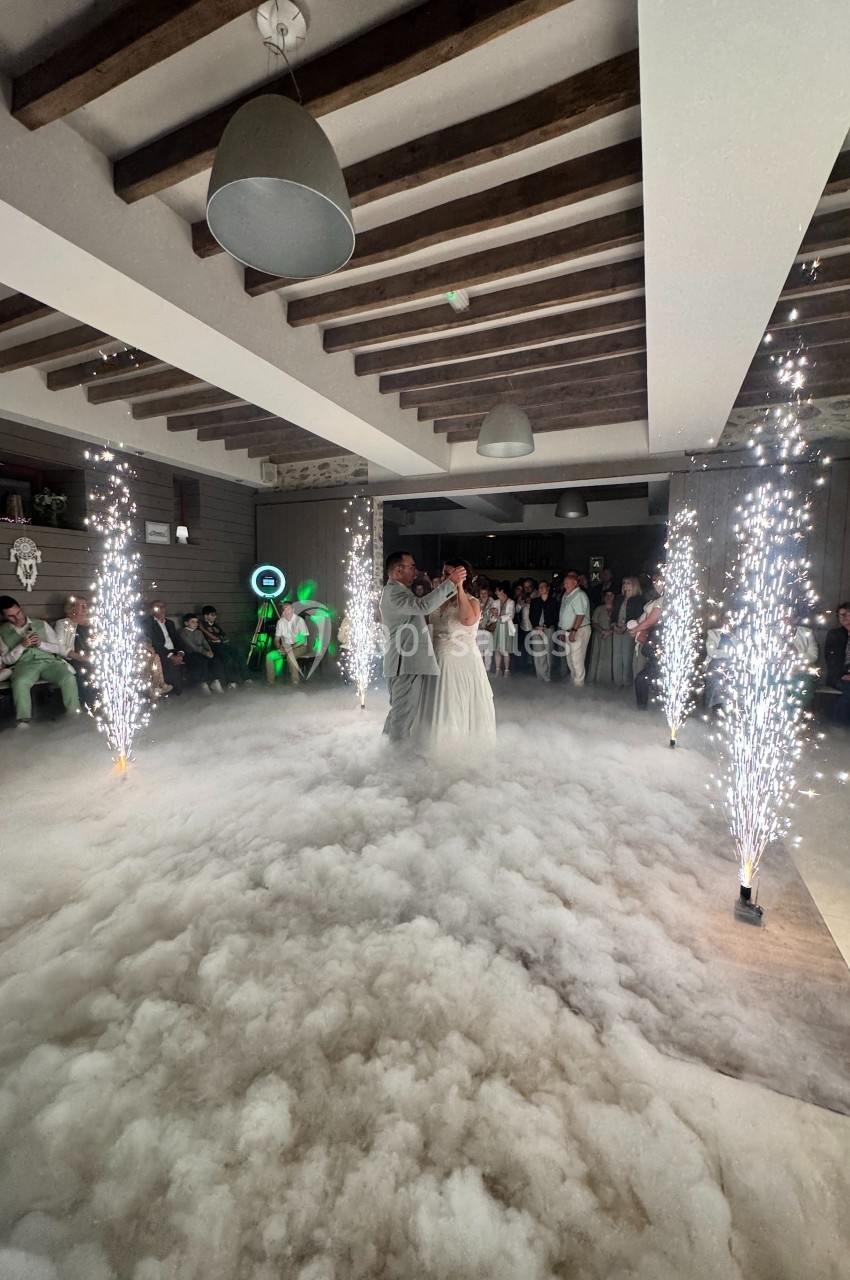 Un couple danse au milieu d'une piste recouverte de fumée, entourée de fontaines d'étincelles, sous un plafond en poutres…