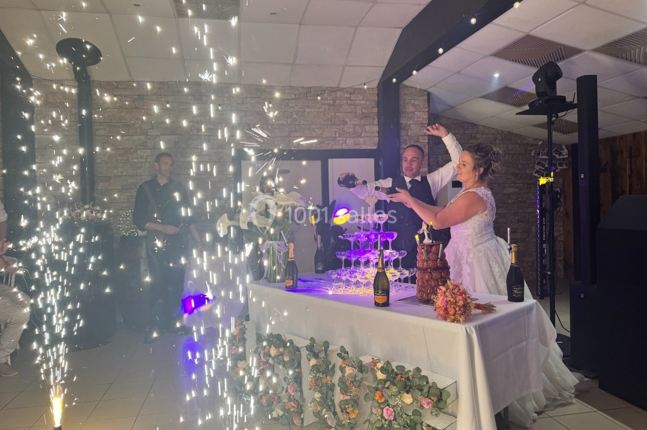 Un couple de mariés verse du champagne dans une pyramide de verres, entouré de décorations et d'effets lumineux.