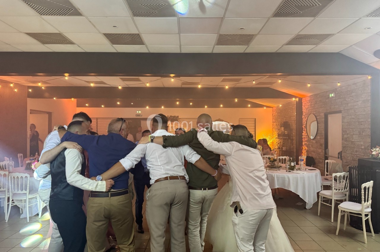 Groupe de personnes formant une ronde dans une salle de réception décorée, éclairée par des lumières chaleureuses.