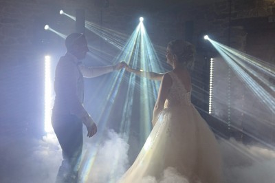 Un couple pose près d'une table décorée de fleurs et d'une pyramide de coupes de champagne dans une salle éclairée.