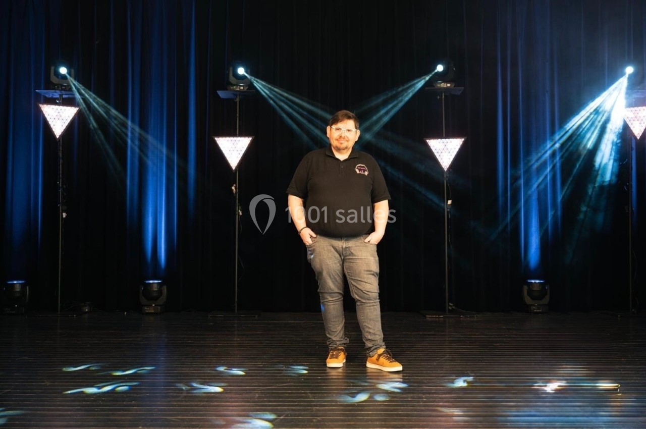 Un homme debout sur une scène sombre éclairée par des projecteurs et des faisceaux lumineux bleus.