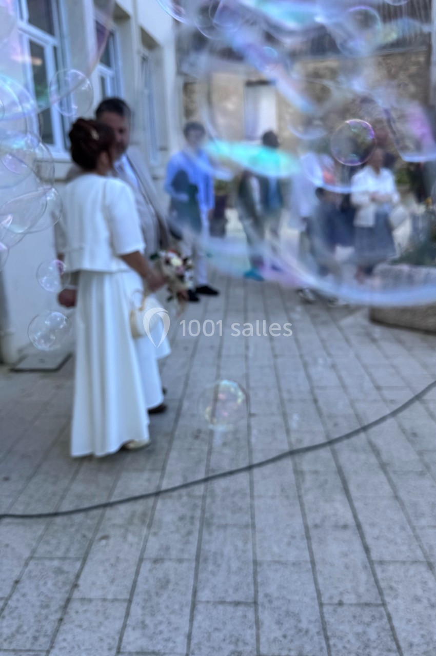 Un couple en tenue de mariage se tient debout à l'extérieur, entouré de bulles de savon.