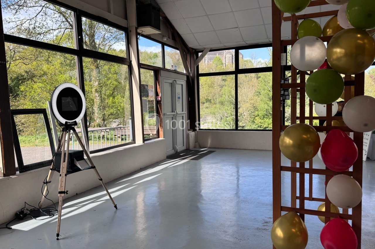 Salle lumineuse avec de grandes baies vitrées, un trépied avec un anneau lumineux et une structure décorée de ballons.